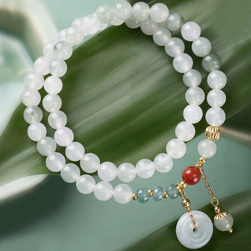 Green jade peace buckle double wrap bracelet flat lay on leaf backdrop with red agate and gold hardware