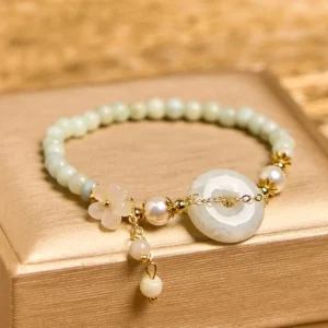 Matte light green jade peace buckle bracelet on wooden tray showing central peace buckle pendant and dangling pearl bead charms