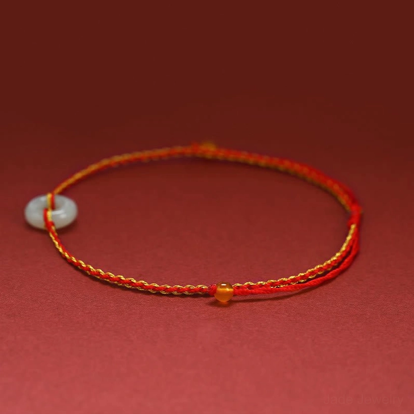Single jade peace buckle bracelet anklet in side flat lay position, showing red braided cord and jade charm accent bead