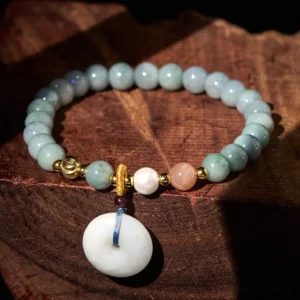 Light blue jade peace buckle bracelet flat lay with gold spacers and white jade pendant on dark wooden surface