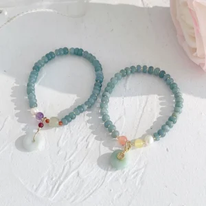 Pair of jade beaded prosperity bracelets with peace buckle pendants and colorful accent beads on textured white surface