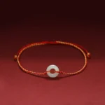 Jade peace buckle braided bracelet with red string, featuring round white jade charm on premium braided cord, front view