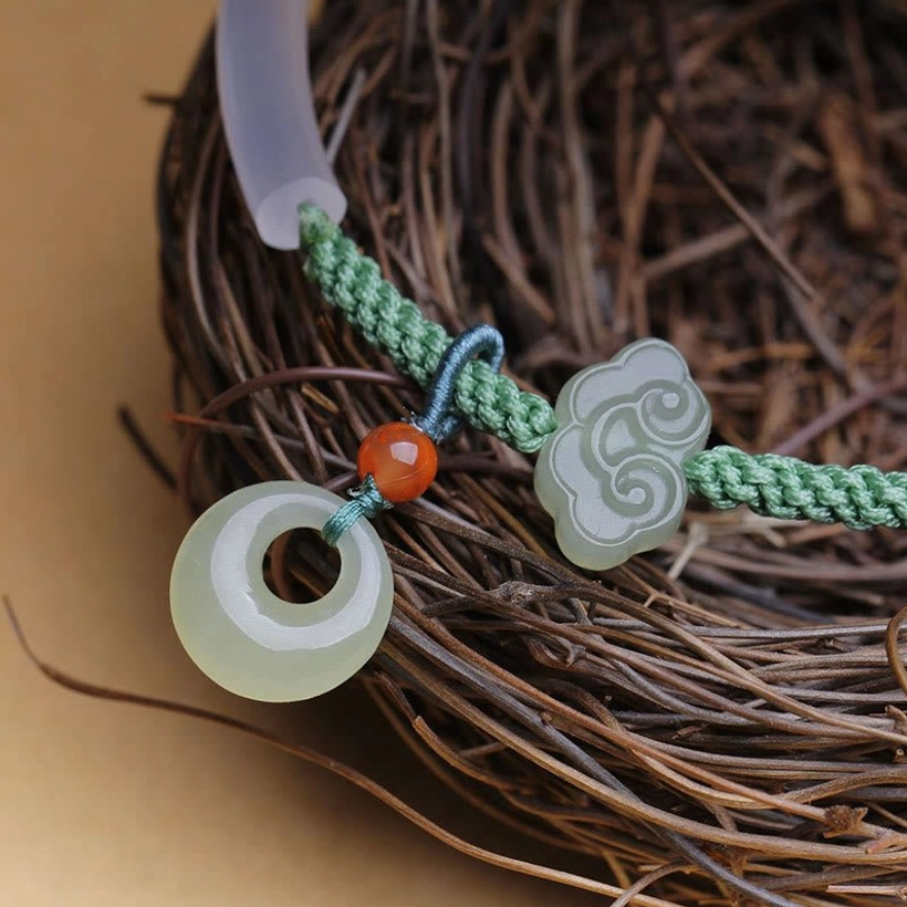 Close-up side view of jade peace buckle bracelet on natural twig nest, detailed view of braided cord and jade decorations