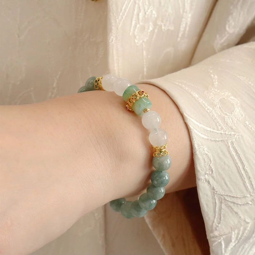Single strand jade bracelet side view showcasing dark green jade beads with white round jade beads and gold spacers on embroidered clothing