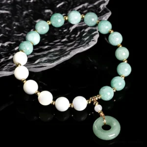 Jade peace buckle prosperity bracelet side oblique flat lay displayed on textured stone slab showing green jade beads and trochus charm