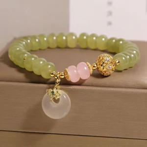Natural jade beaded bracelet with rose quartz and carved peace buckle pendant displayed from three-quarter angle