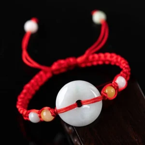 Milky white jade peace buckle red string bracelet displayed on dark wooden surface with golden silk jade accent beads and adjustable rope closure