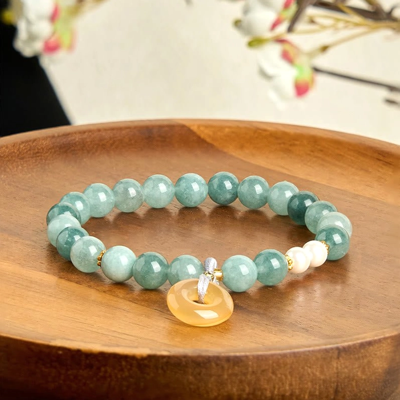 Two-tone green jade peace buckle bracelet with pearls and yellow jade charm on decorative wooden tray with floral backdrop