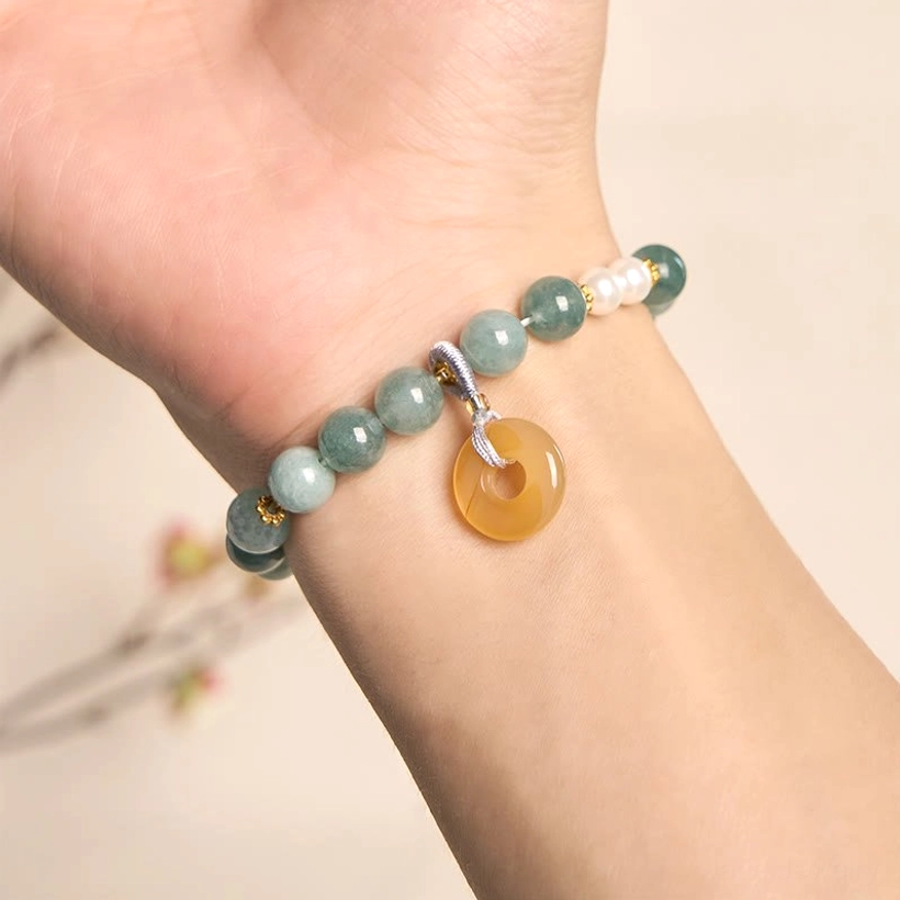 Jade peace buckle bracelet worn on left wrist in lifestyle setting, showing jade beads, white pearls, and yellow peace buckle pendant