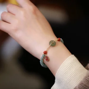 Natural jade and red agate peace buckle bracelet worn on wrist with beige knit sleeve - side view