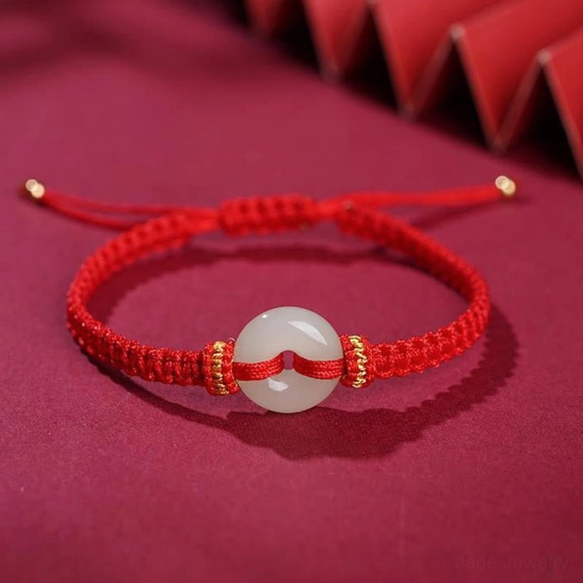 Top-down view of bright red braided peace buckle jade bracelet with white jade pendant and gold decorative knots