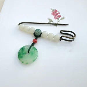 Jade peace buckle safety pin brooch flat lay with red accent bead and dual-part metal design on white paper