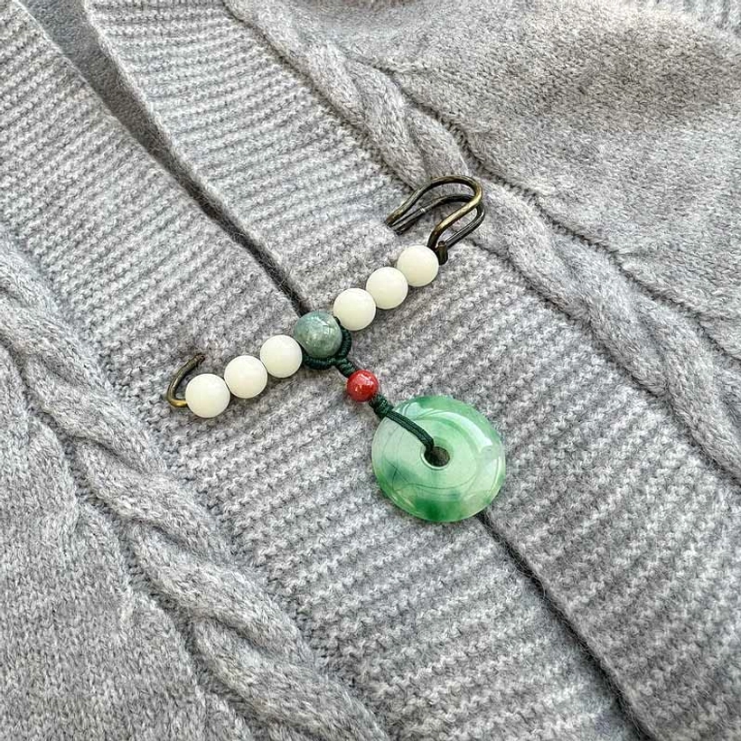 Jade peace buckle brooch styled on grey cable-knit sweater showing protective symbol and red bead accent