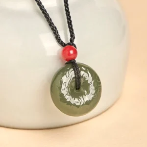 Close-up side view of carved cyan jade peace buckle pendant with embossed dragon pattern and black cord with red bead