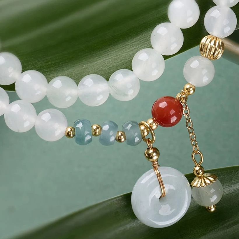 Detailed close-up of jade bracelet gold clasps beads and peace buckle charm on leaf background