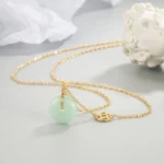 Jade peace buckle fu character necklace with light green jade donut pendant and gold fu coin charm on delicate gold chain, overhead tabletop styling