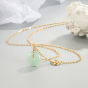 Jade peace buckle fu character necklace with light green jade donut pendant and gold fu coin charm on delicate gold chain, overhead tabletop styling