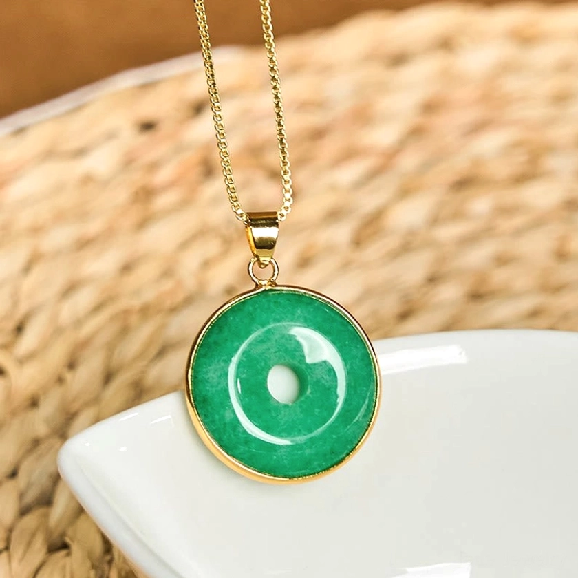 Natural cyan jade peace buckle with gold setting - top-down view on ceramic tray highlighting pendant design