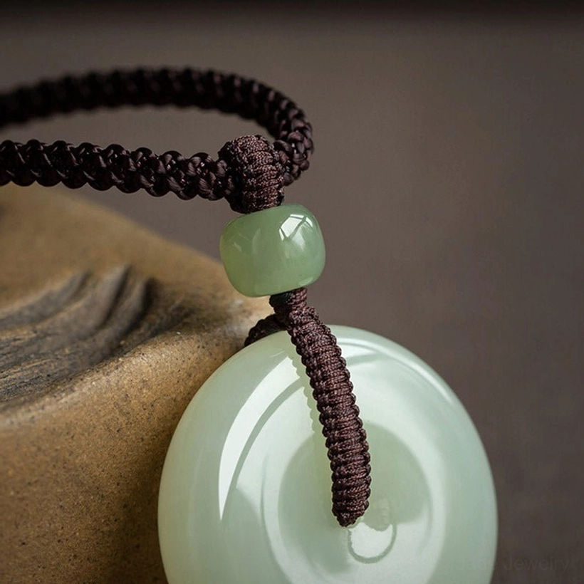 Macro close-up of jade peace buckle pendant showing thick braided woven cord knot and green spacer bead detail