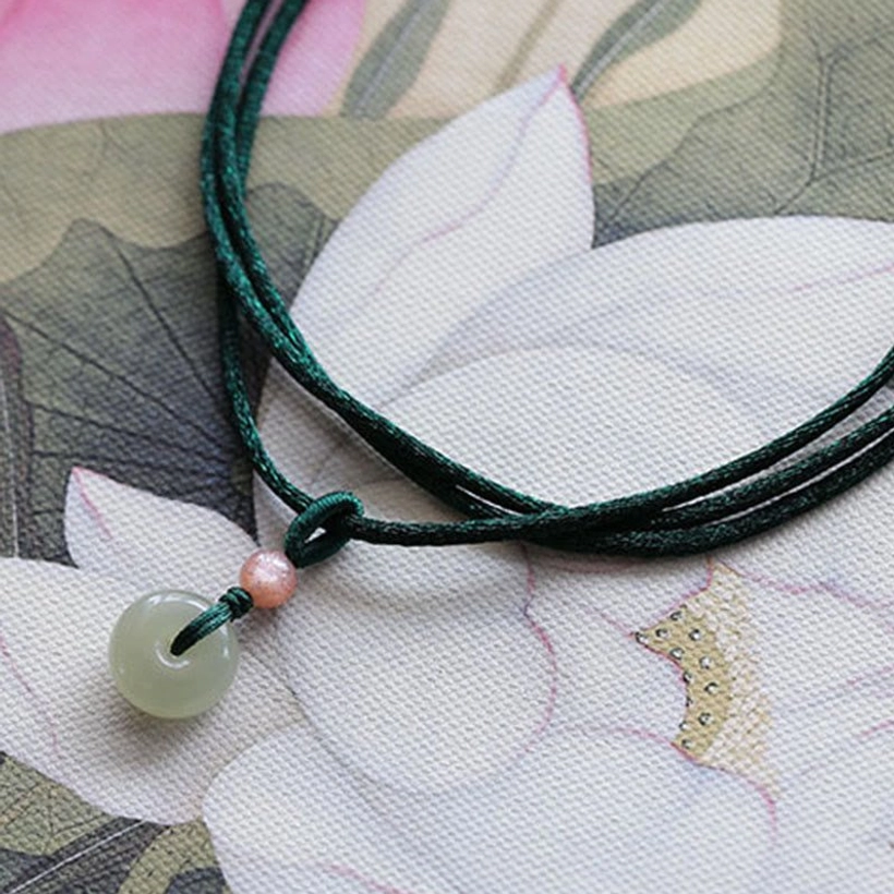 Jade peace buckle necklace with dark green double wax cord on lotus painting background, flat lay