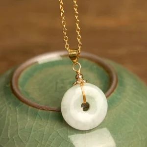 Authentic light green jade peace buckle necklace pendant displayed on green ceramic coaster, showing polished milky jade donut with twisted gold decorative bail and delicate gold cable chain