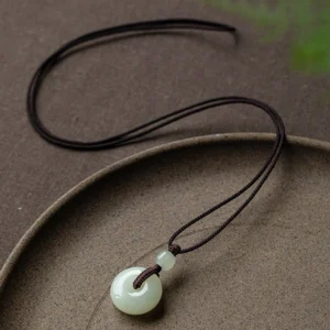 Natural jade peace buckle necklace with dark brown woven cord displayed on ceramic tray showing celadon green jade pendant
