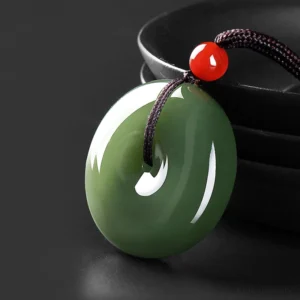Natural round jade peace buckle necklace pendant in deep emerald green with red accent bead and black braided rope, three-quarter close-up view