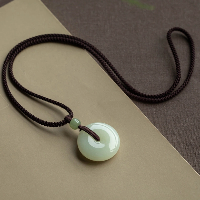 Natural jade peace buckle pendant necklace flat lay on paper mat showing celadon jade and traditional woven cord