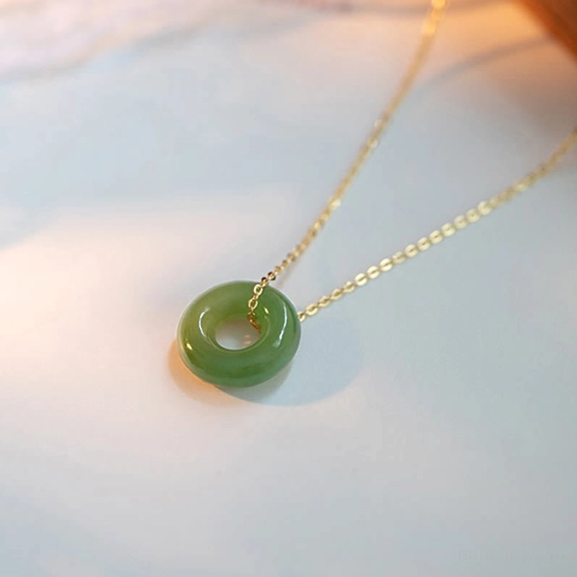 Three-quarter side view of green Hetian jade peace buckle necklace with warm studio lighting highlighting the gold-plated chain