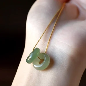 Natural jade peace buckle pendant necklace on wrist, light green polished jade with delicate gold-plated sterling silver chain close-up