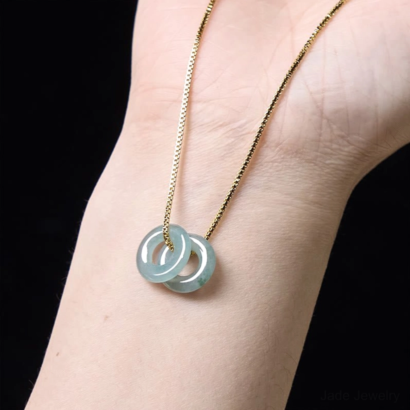 Double jade peace buckle necklace positioned on inner wrist, light blue-green jade with chain detail