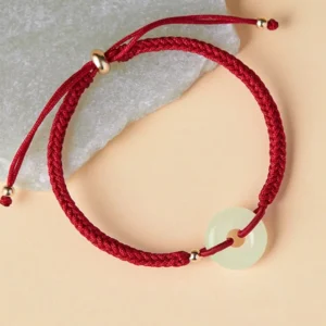 Close-up view of jade peace buckle pendant on braided red rope with gold spacer beads