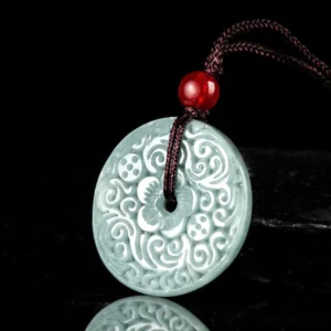 Close-up front view of hand-carved jade peace buckle showing symmetrical floral engravings with brown cord and red accent bead