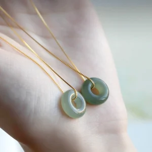 Two natural jade peace buckle necklaces in palm, light and medium green jade donut pendants displaying jade color variations