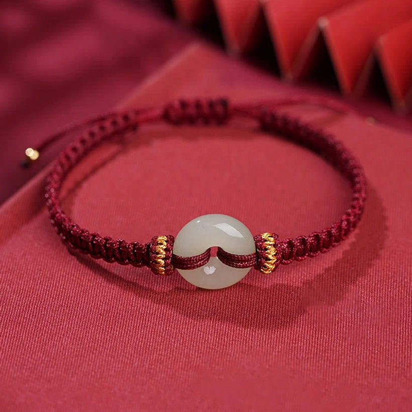Top-down flat lay of adjustable jade peace buckle bracelet with wine-red braided cord, gold decorative knots, and pull tab closures