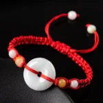 Jade peace buckle red string bracelet on black background showing light green jade donut pendant with mixed decorative beads and adjustable braided rope