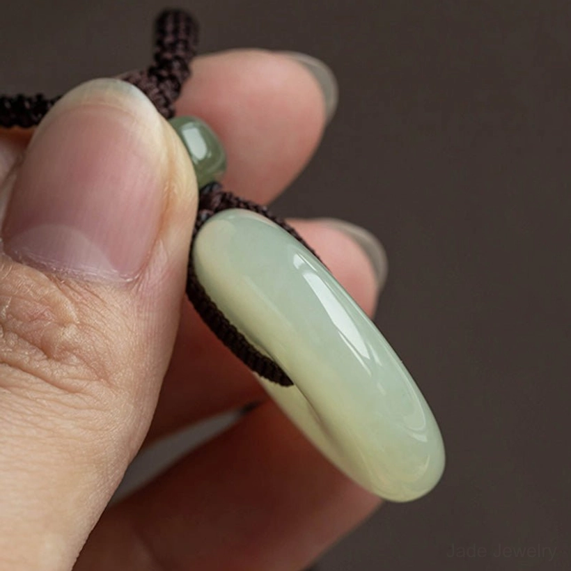 Jade peace buckle pendant side profile held on fingertip showing smooth curved ring and traditional woven knot