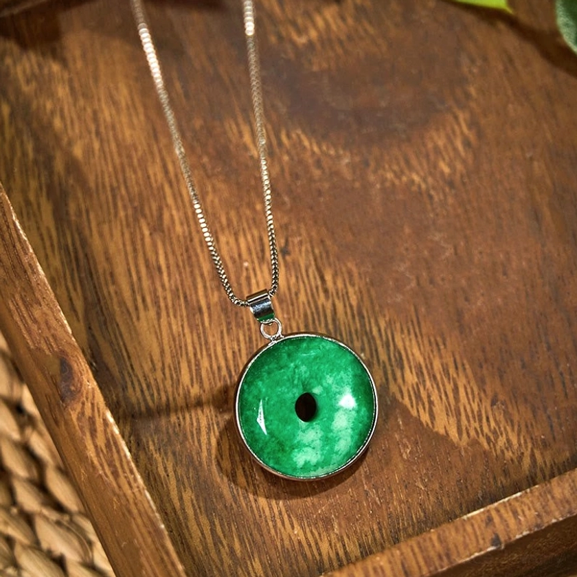 Silver-toned jade peace buckle with emerald-green pendant - angled top-down view on dark wooden surface