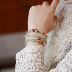 Jade pearl butterfly bracelet layered stack worn on wrist, close-up detail shot displaying mixed bead designs with gold and red charm ornaments on lace clothing