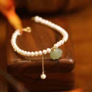 Natural Hetian jade cat paw bracelet with pearl strand displayed flat on wooden base, showing premium gold-filled buckle and adjustable design