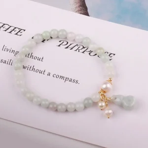 Overhead flat lay of natural jade pearl gourd luck bracelet on book page showing smooth jade beads, gold fittings, and pearl gourd pendant