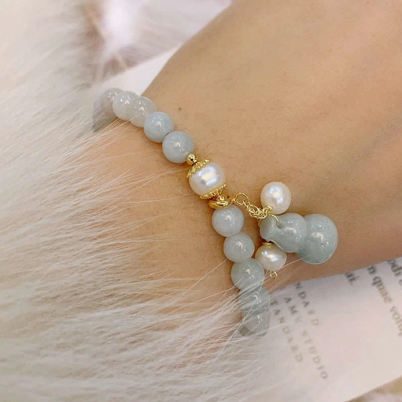 Close-up of jade pearl gourd bracelet worn on wrist with pale blue-green jade beads and gold hardware on faux fur background