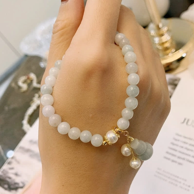 Natural jade pearl gourd luck bracelet worn on hand showing light jade round beads, gold hardware, and pearl gourd pendant on decorative table