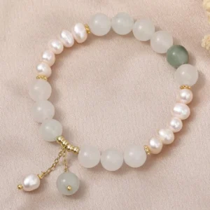 Handmade jade pearl bracelet flat lay showing beaded stretch design with matte white jade, small pearls, and decorative gold dangle