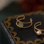 Double layer jade pearl adjustable ring with twisted gold bands on vintage leather backdrop, top-down side view showcasing cuff design