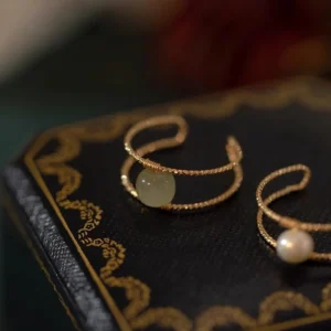 Double layer jade pearl adjustable ring with twisted gold bands on vintage leather backdrop, top-down side view showcasing cuff design