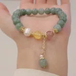 Jade pearl strawberry quartz prosperity bracelet worn on wrist, overhead view showing mixed gemstone beads with dangling jade pendant charm and gold-toned hardware