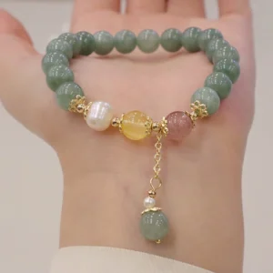 Jade pearl strawberry quartz prosperity bracelet worn on wrist, overhead view showing mixed gemstone beads with dangling jade pendant charm and gold-toned hardware