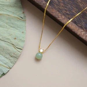 Handcrafted jade bead pendant necklace with delicate gold chain and zirconia accent, flat lay top view with lotus leaf styling