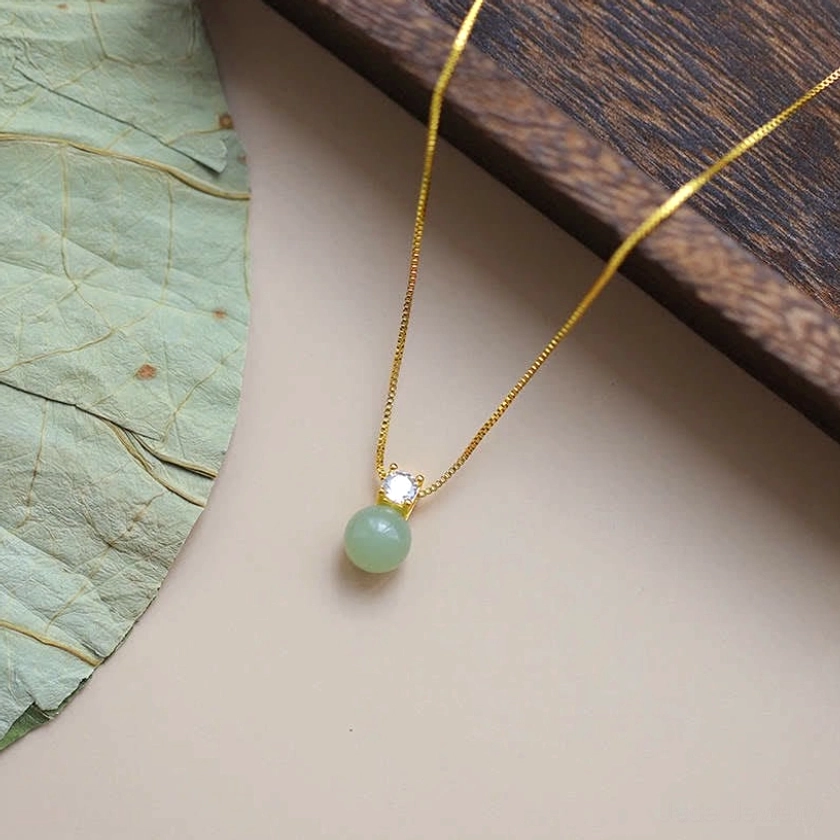 Handcrafted jade bead pendant necklace with delicate gold chain and zirconia accent, flat lay top view with lotus leaf styling